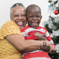 Grandmother hugging grandson near Christmas tree smiling at camera, close up.